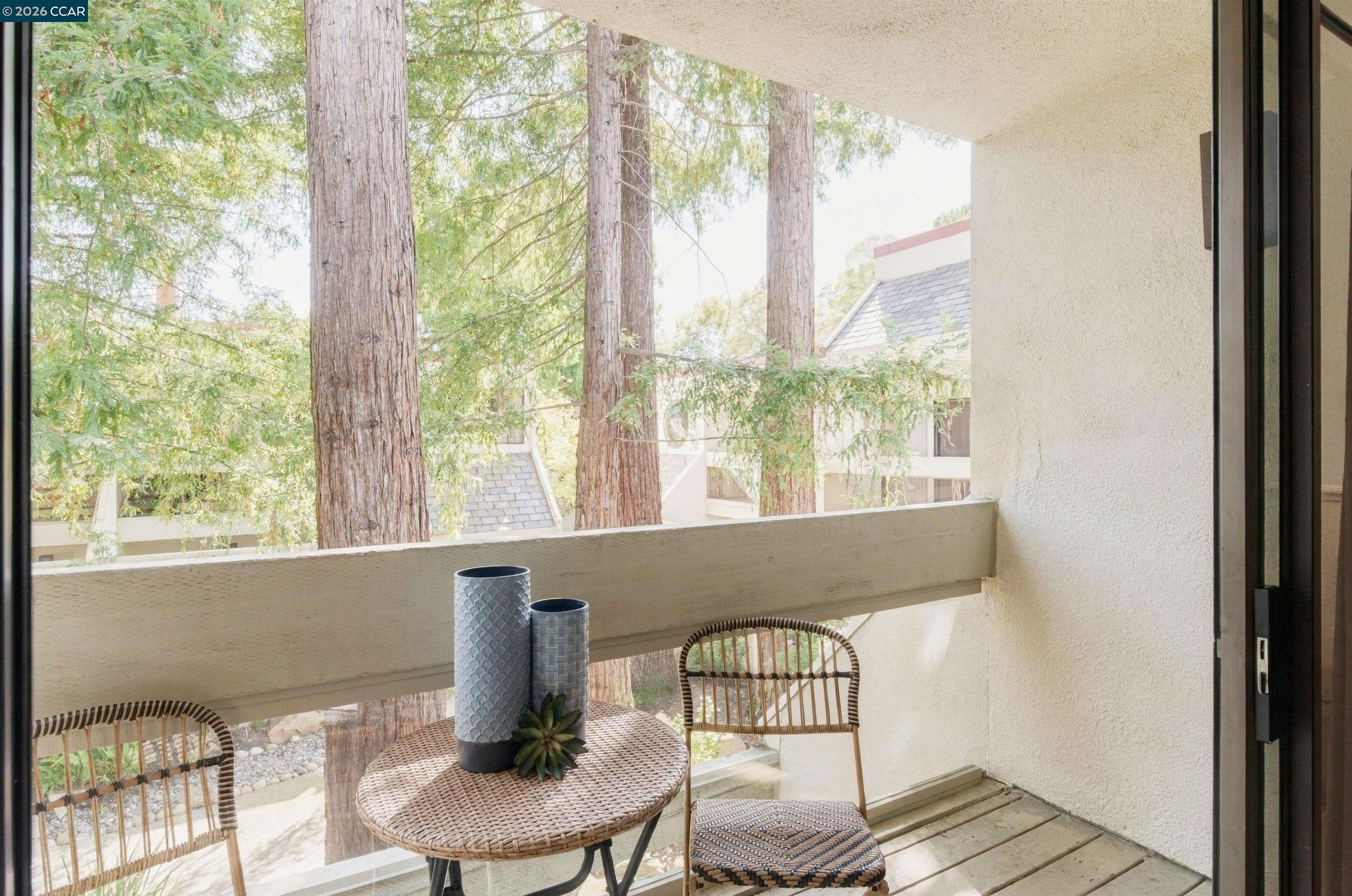 Covered balcony with wicker seating and a view of tall trees.