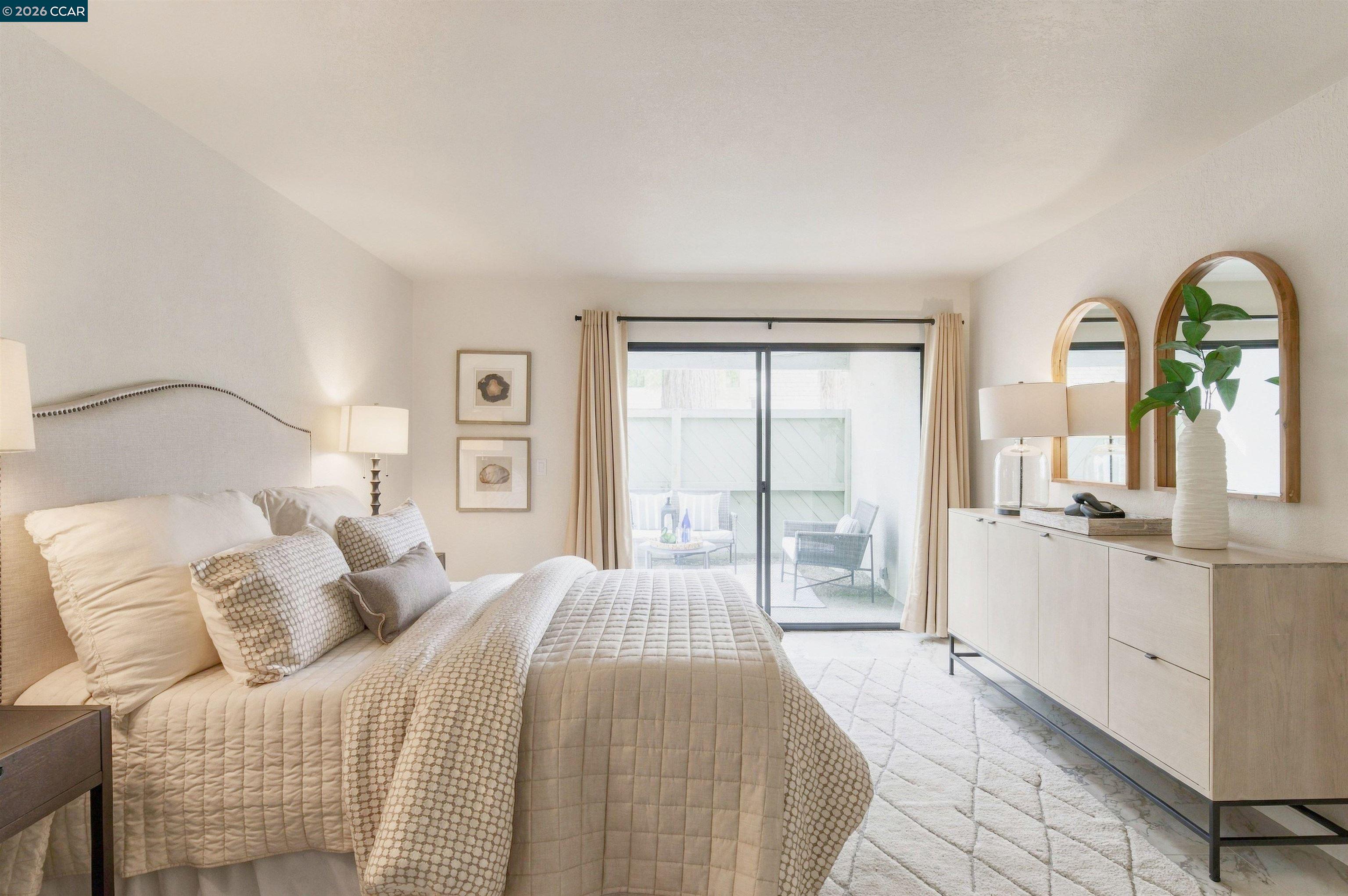 Furnished bedroom with a neutral quilted bed, arched mirrors, and sliding doors to a patio.