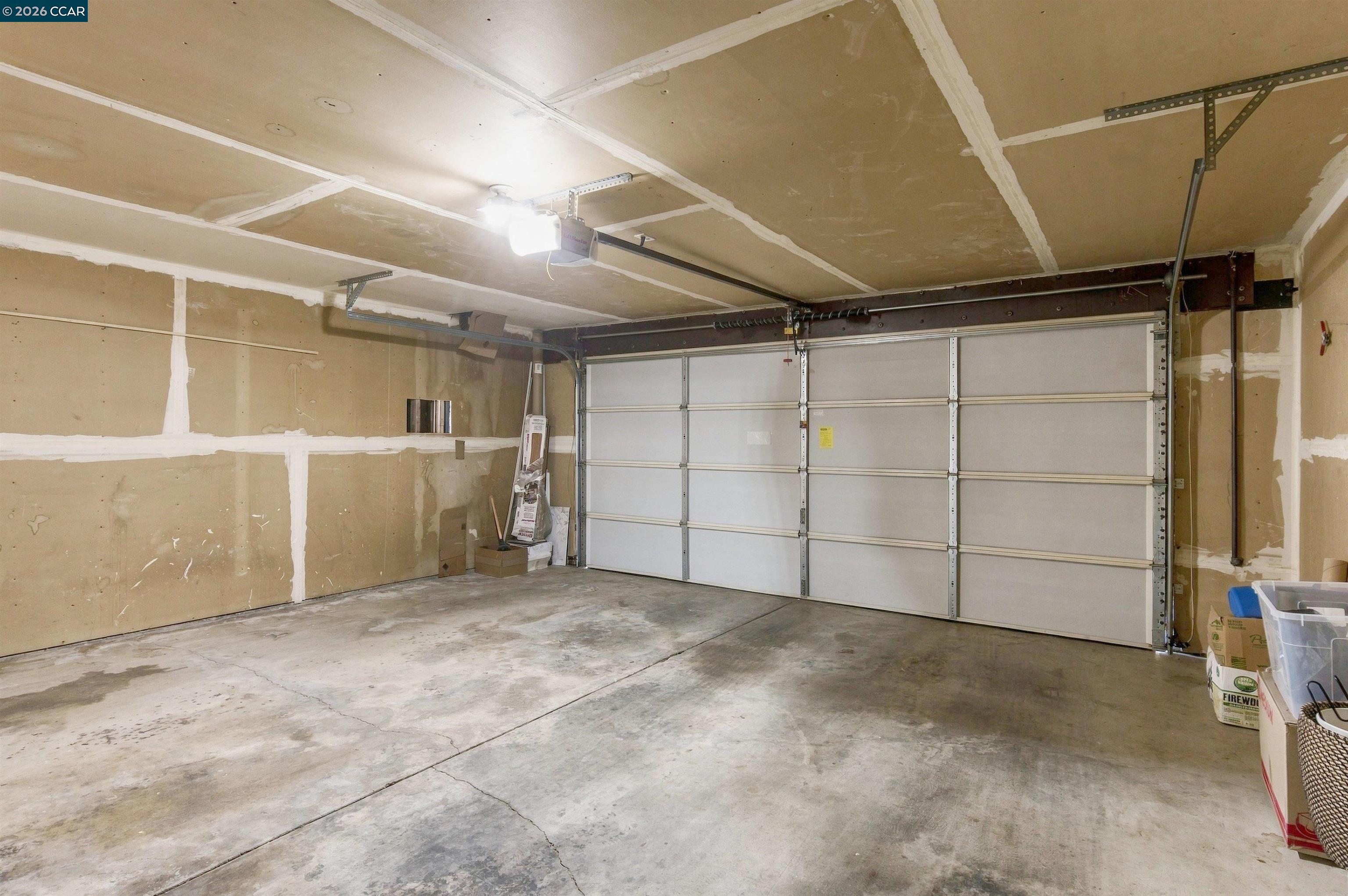 Spacious garage with a closed sectional door, concrete floor, and unfinished drywall.