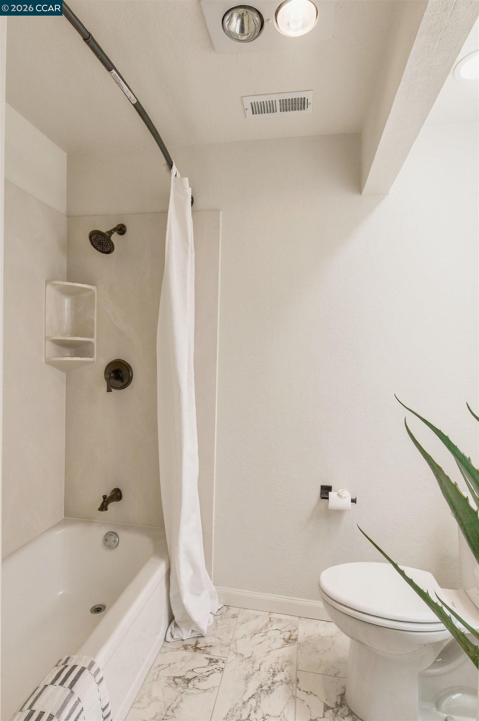 Bathroom with a bathtub, white shower curtain, toilet, and marble-pattern floor tiles.