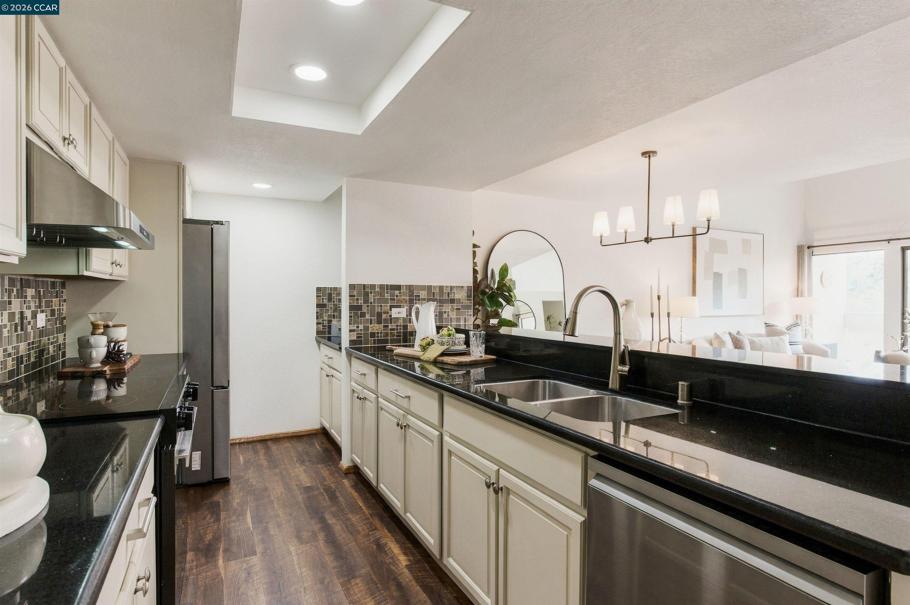 Kitchen with black granite counters, cream cabinets, stainless appliances, and an open view to the living area.