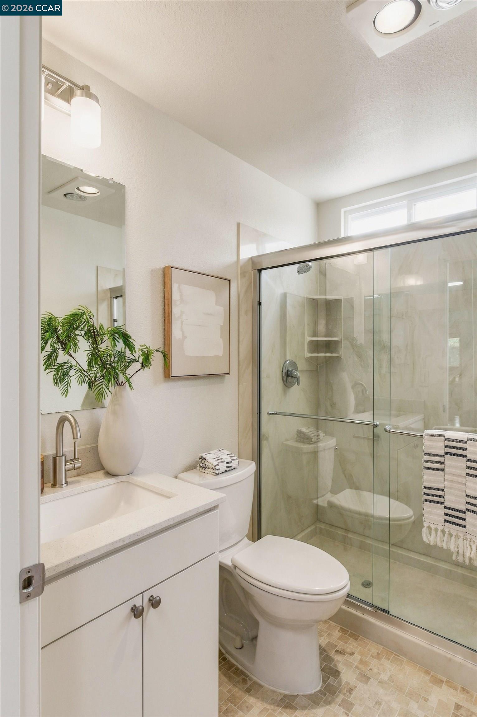 Bathroom with a white vanity and glass-enclosed shower, decorated with a plant and folded towels.