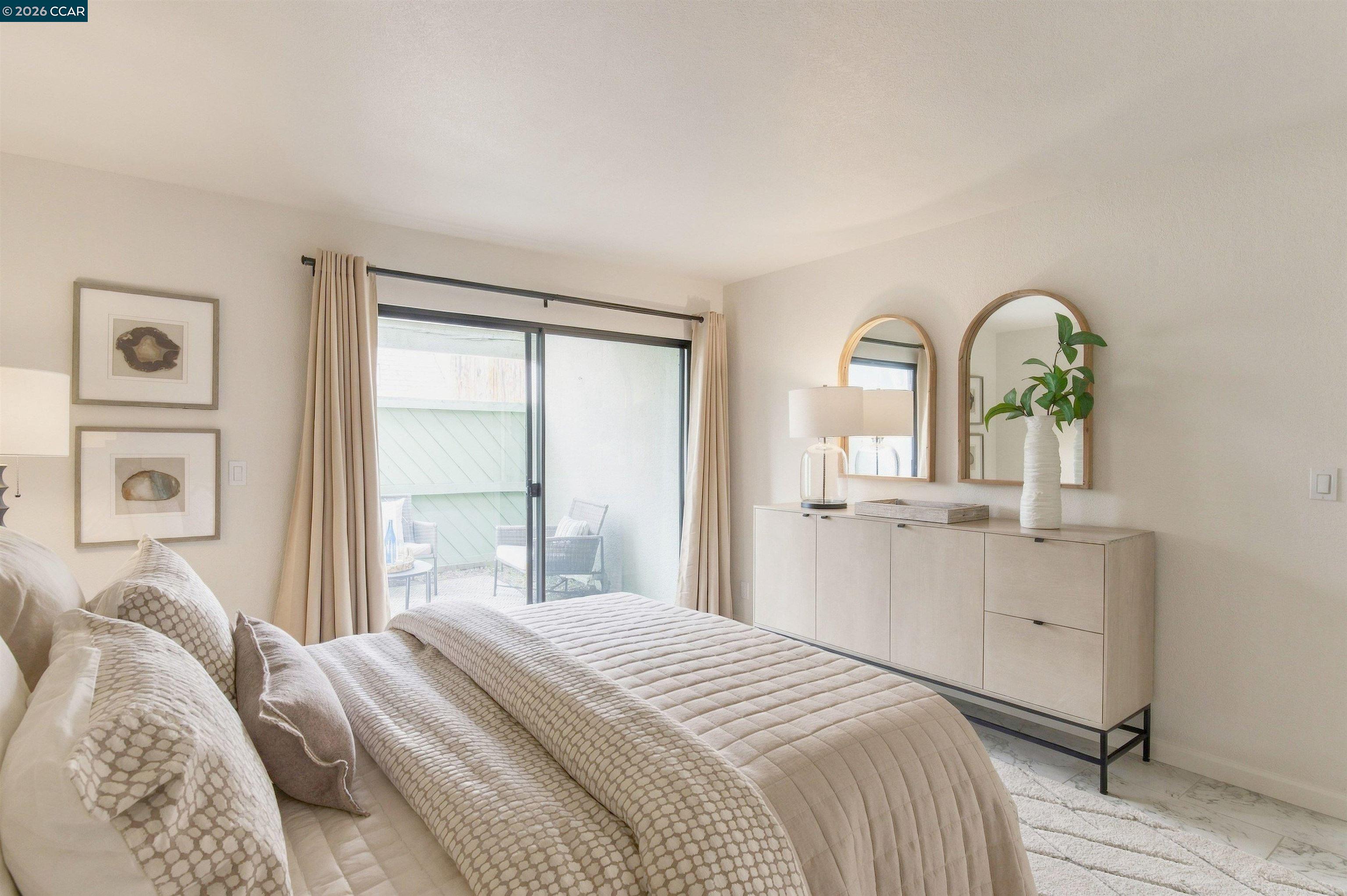 Staged bedroom with a quilted bed, arched mirrors, and sliding doors to a patio.