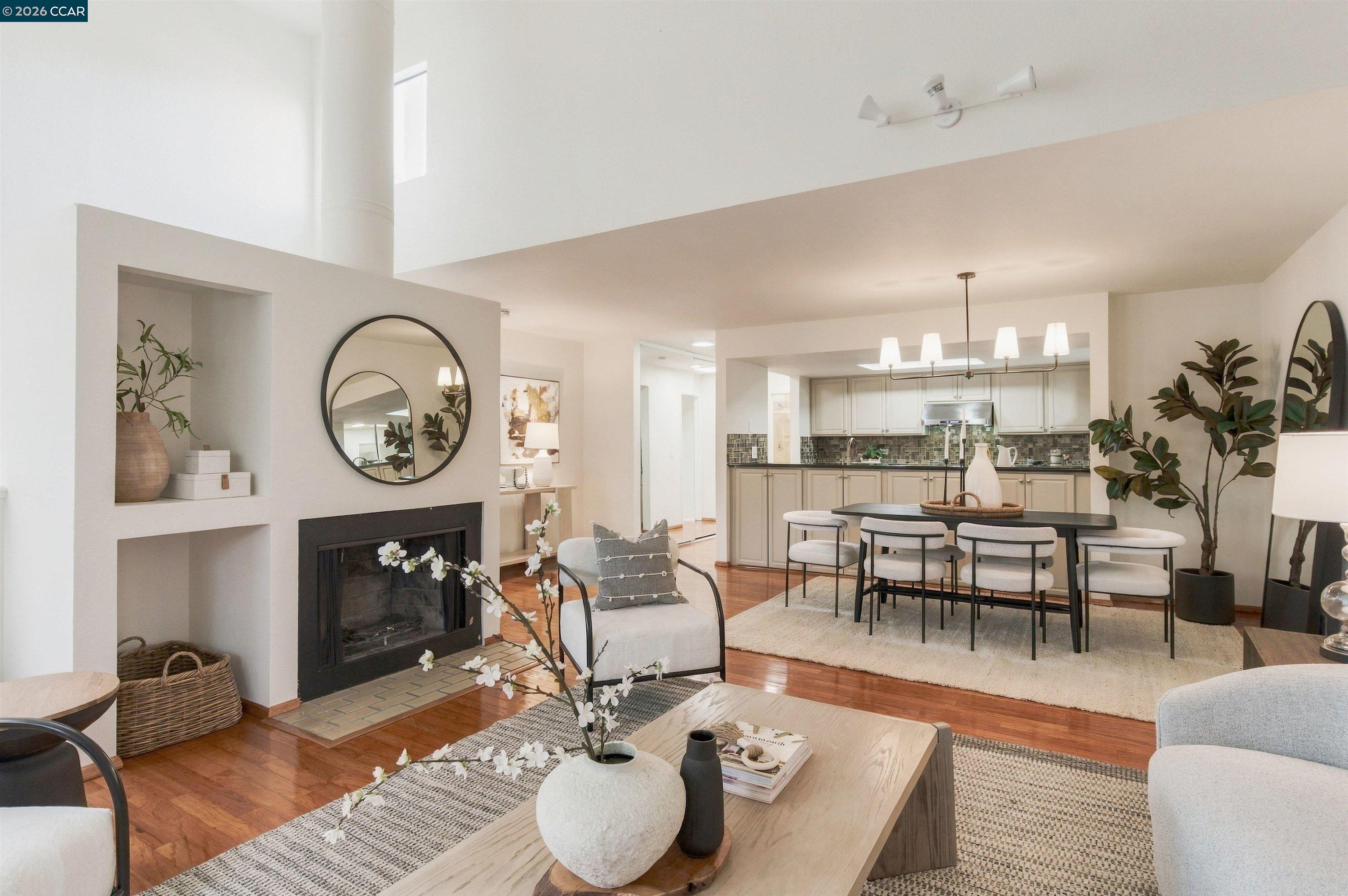 Open-plan living room with a fireplace, hardwood floors, and adjoining dining area and kitchen.