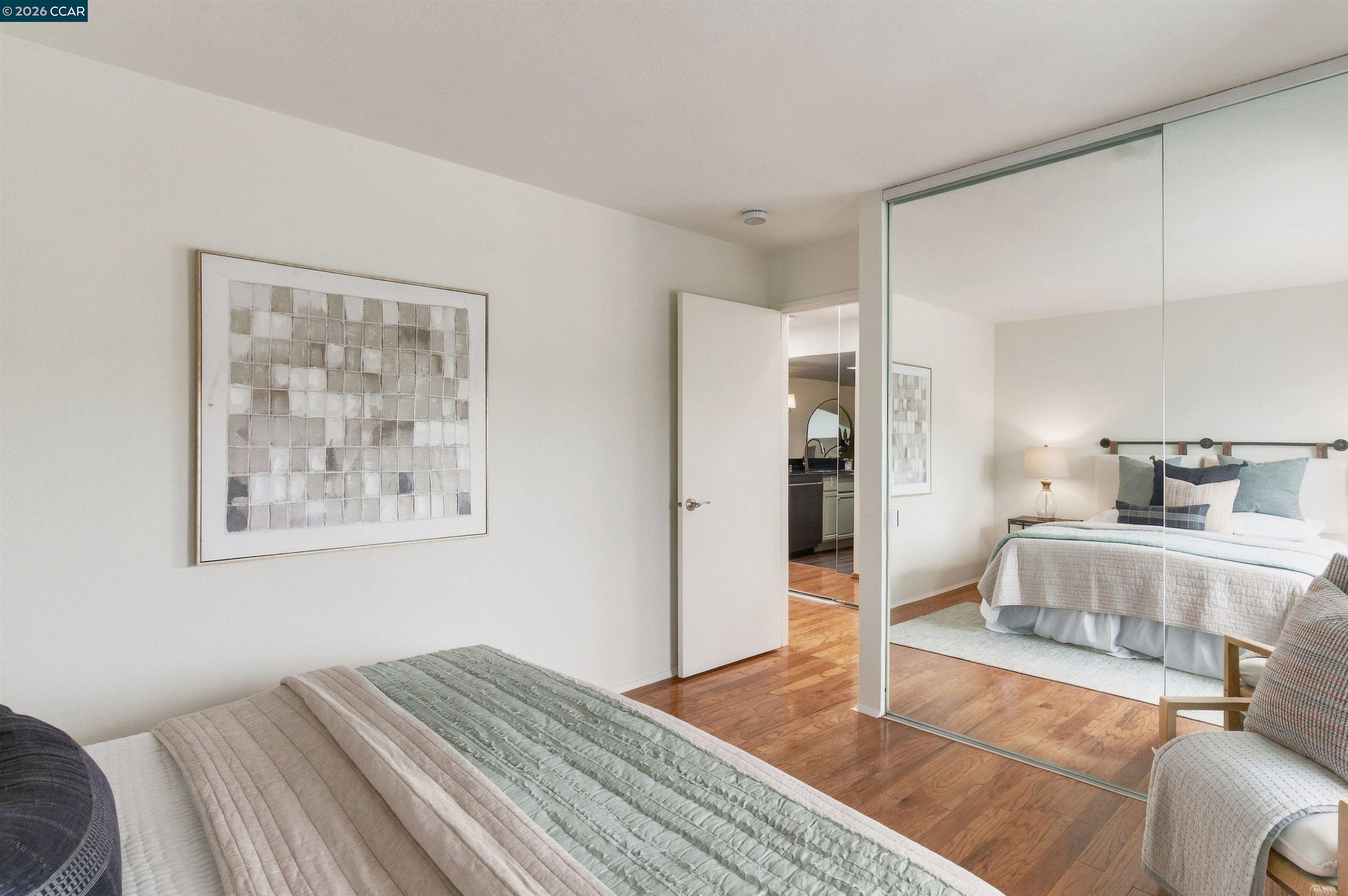 Staged bedroom with hardwood floors and mirrored closet doors reflecting a second bed.
