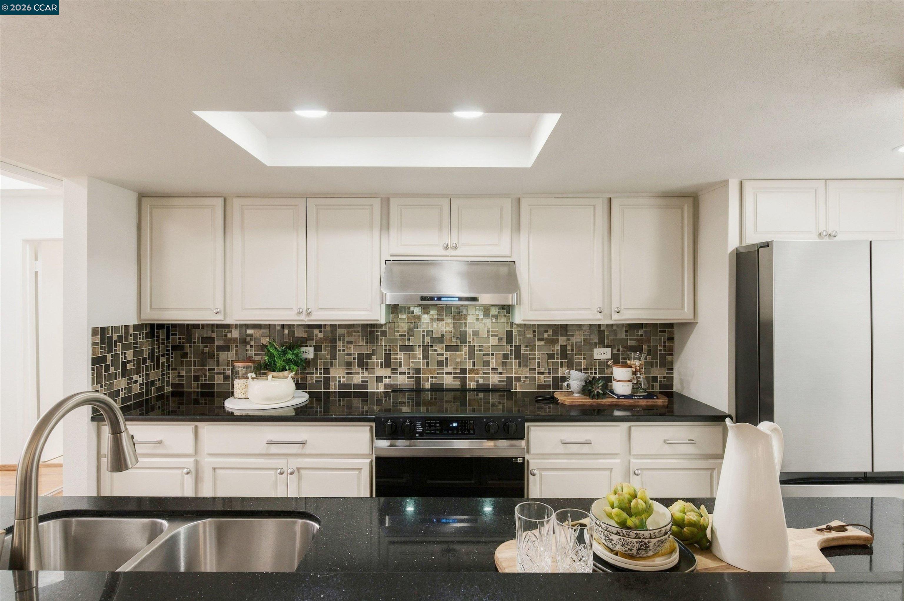 Kitchen with white cabinets, mosaic tile backsplash, black countertops, and stainless steel appliances.