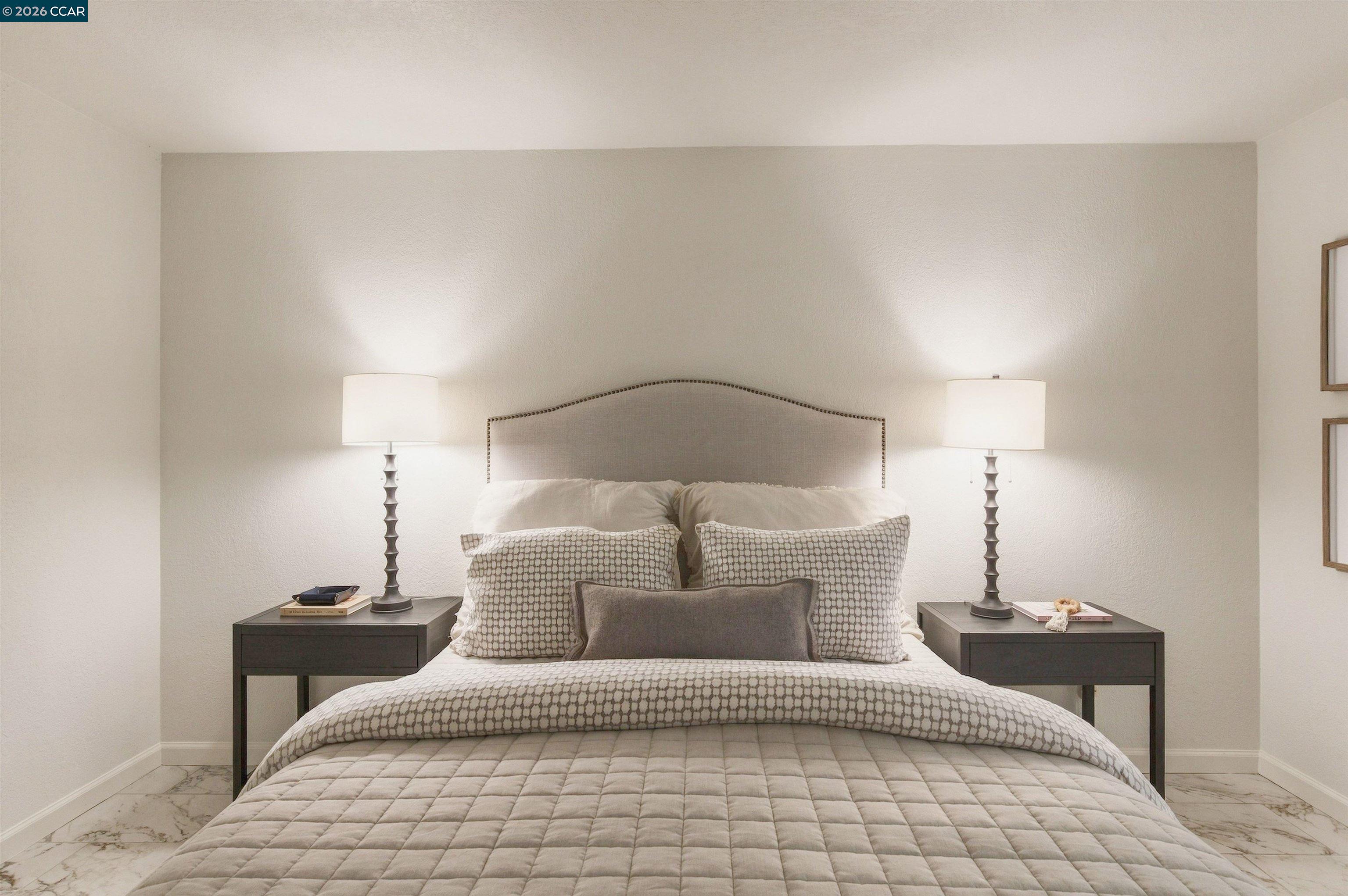 Staged bedroom with a patterned bed, curved upholstered headboard, and matching bedside tables with lamps.