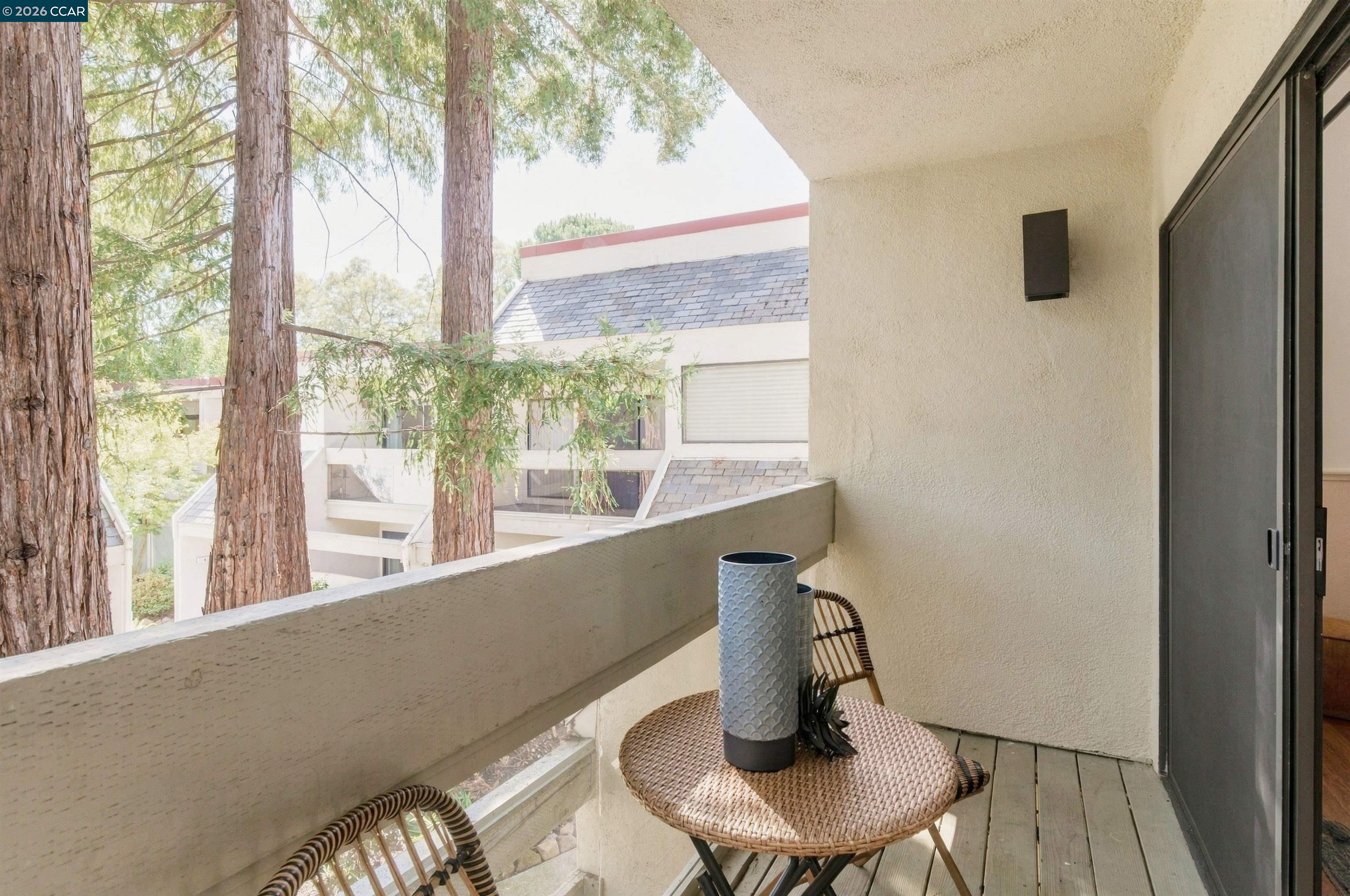 Apartment balcony with woven seating and tall trees visible beyond the railing.