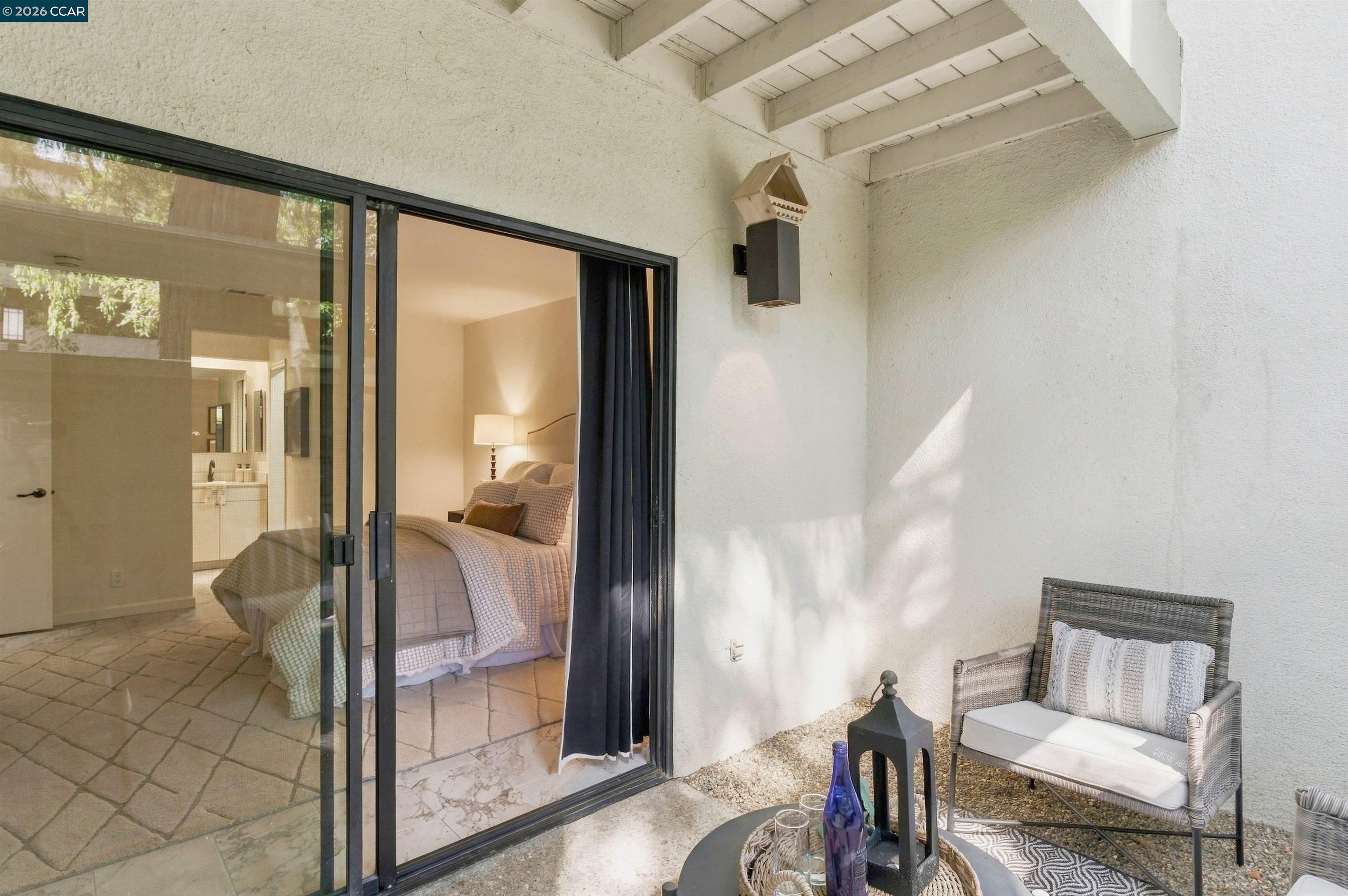 Covered patio with wicker seating beside sliding glass doors opening to a furnished bedroom.