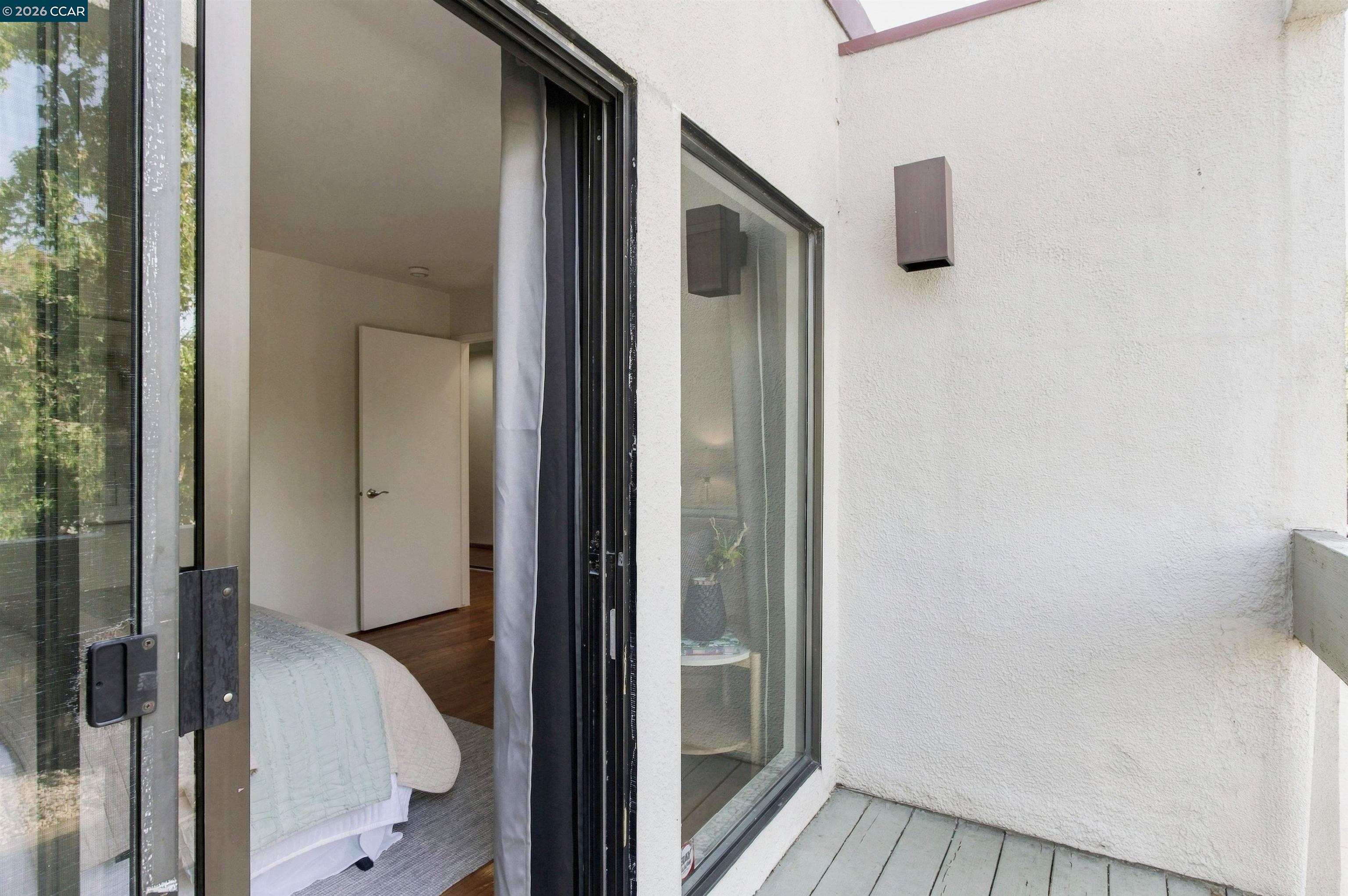 Bedroom with pale bedding visible through an open sliding door onto a small balcony.