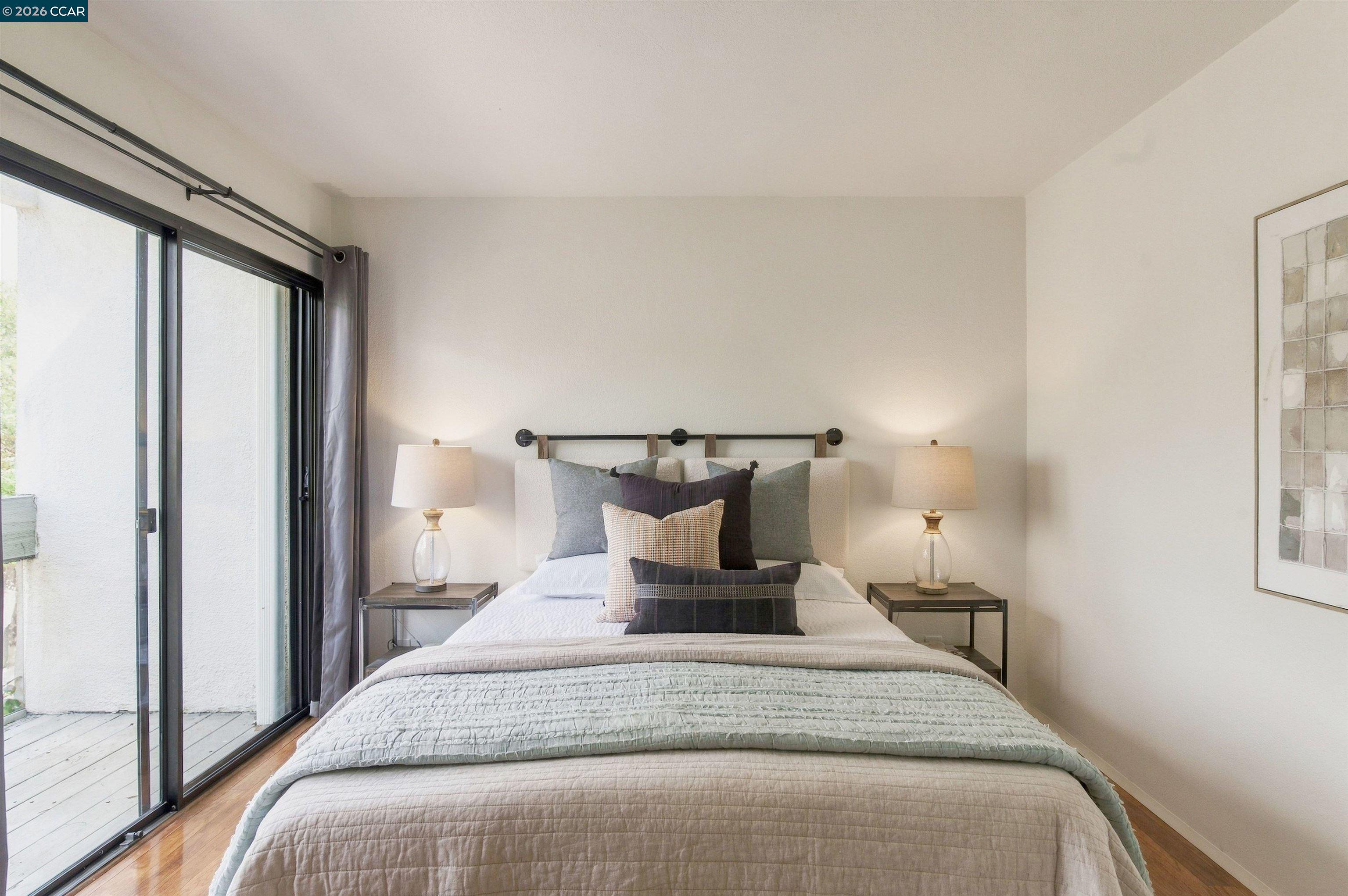 Bedroom with layered pillows, matching bedside lamps, and sliding glass doors opening to a balcony.