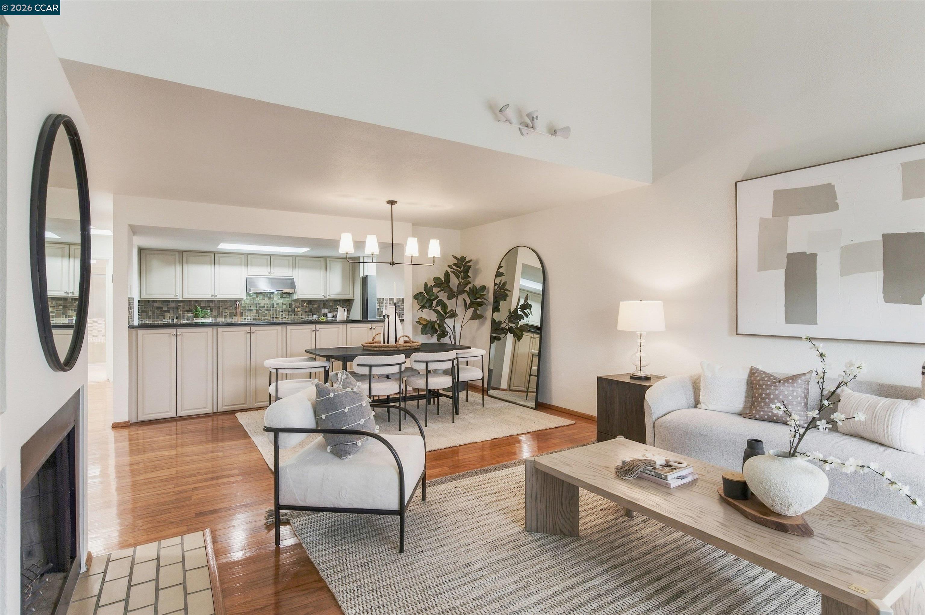 Open-plan living and dining room with a white kitchen, hardwood floors, and neutral furnishings.