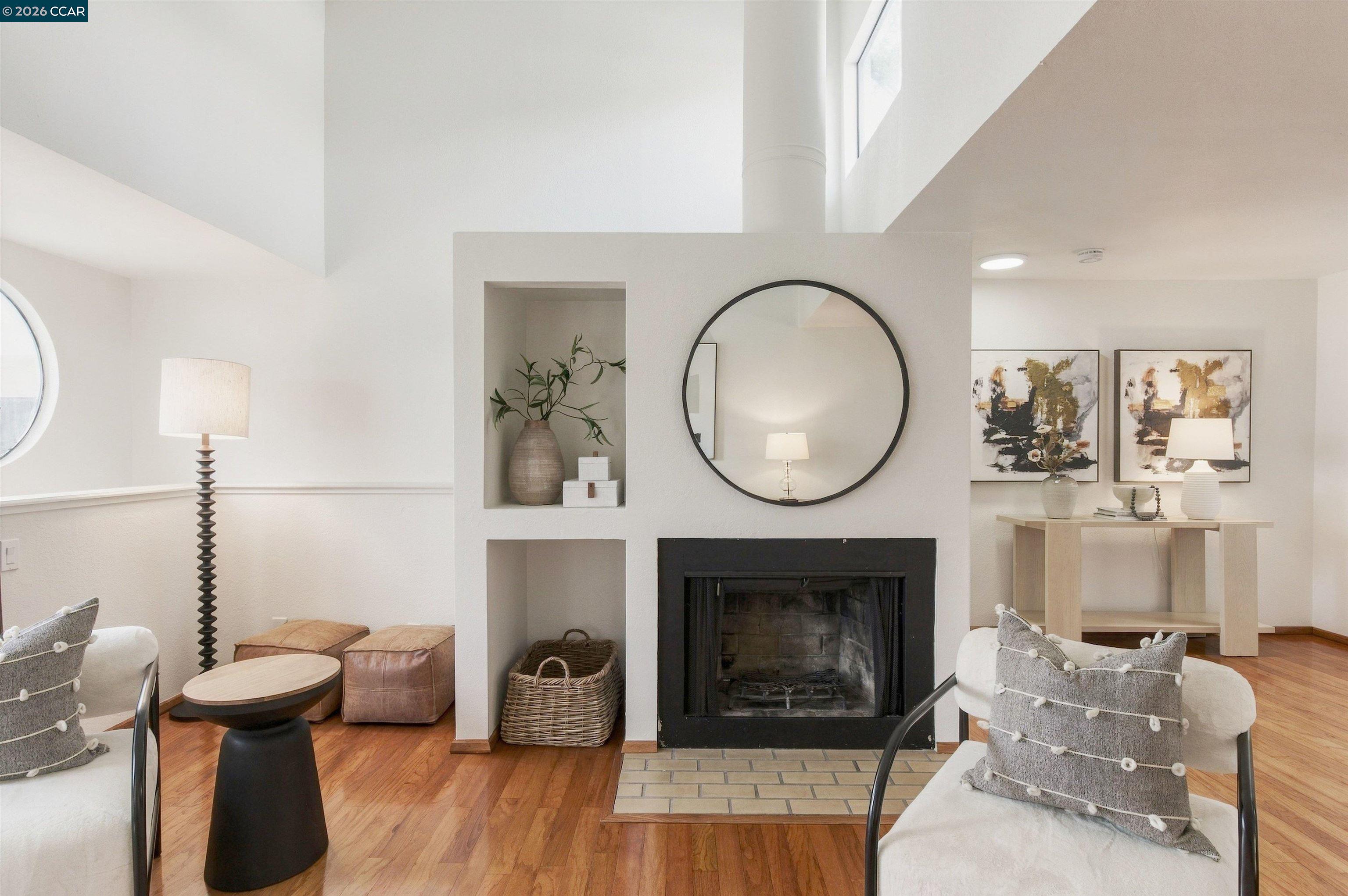 Staged living room with a central fireplace, round mirror, built-in niches, and hardwood floors.