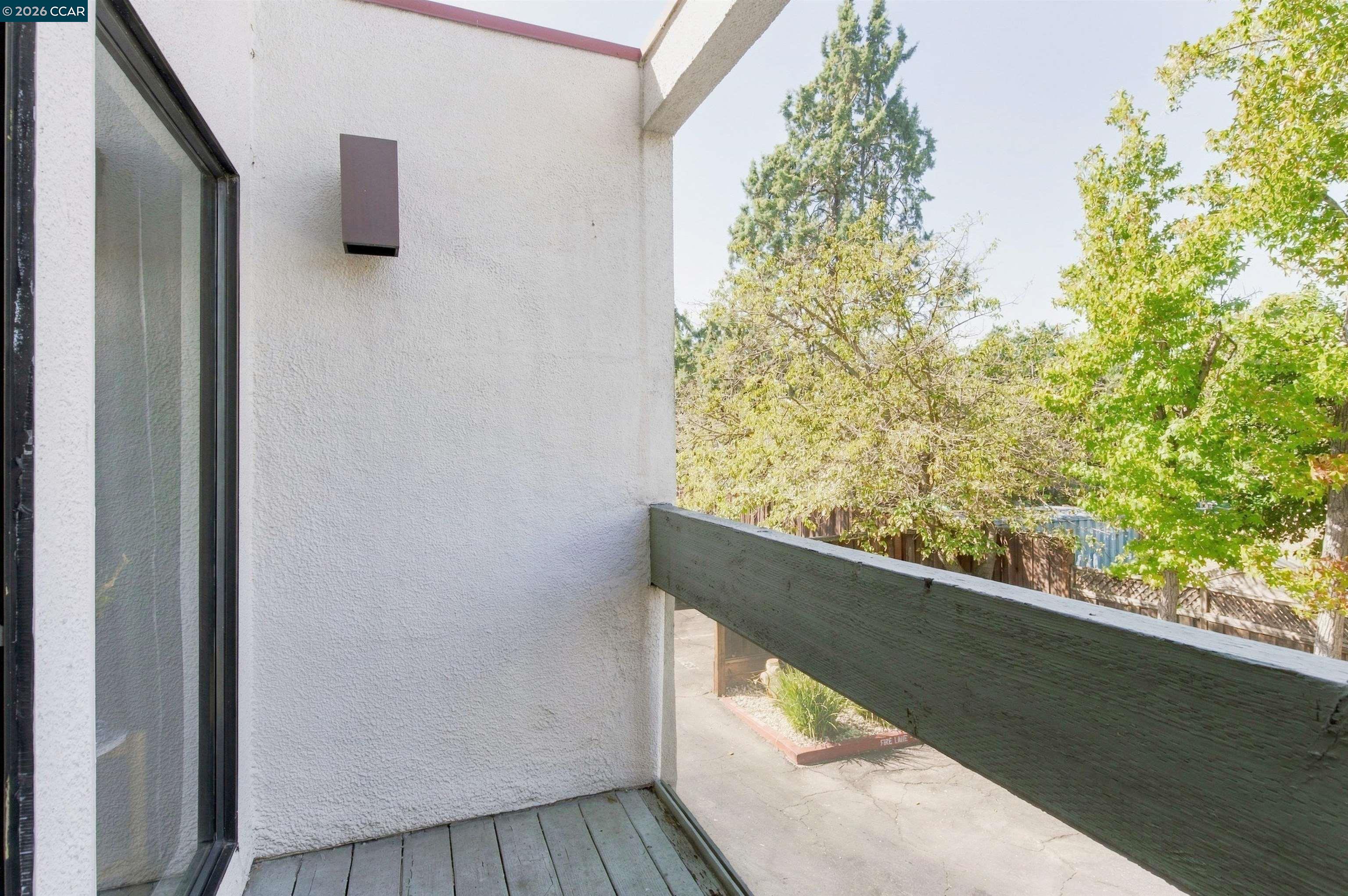 Balcony with gray decking and a dark railing overlooking leafy trees.