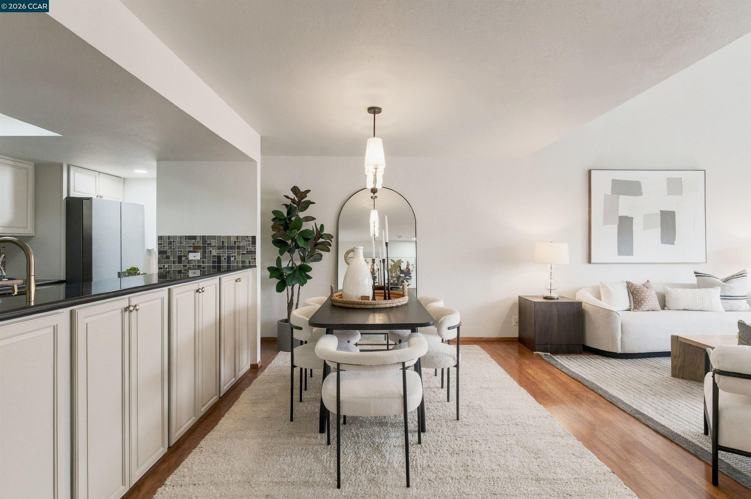 Open-plan kitchen, dining, and living area with white cabinetry and a dark dining table.
