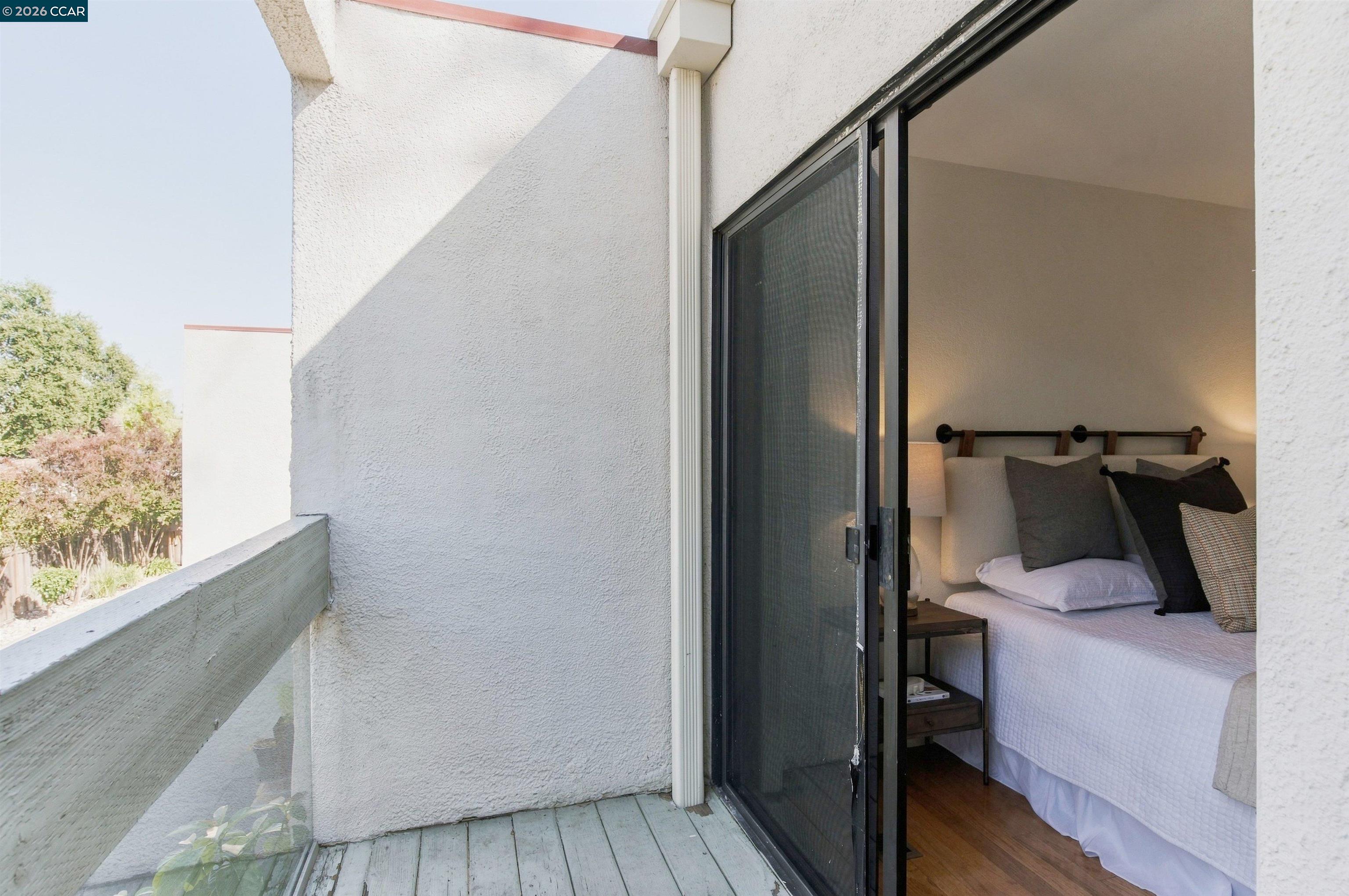 Furnished bedroom with layered pillows opening onto a small balcony through sliding glass doors.