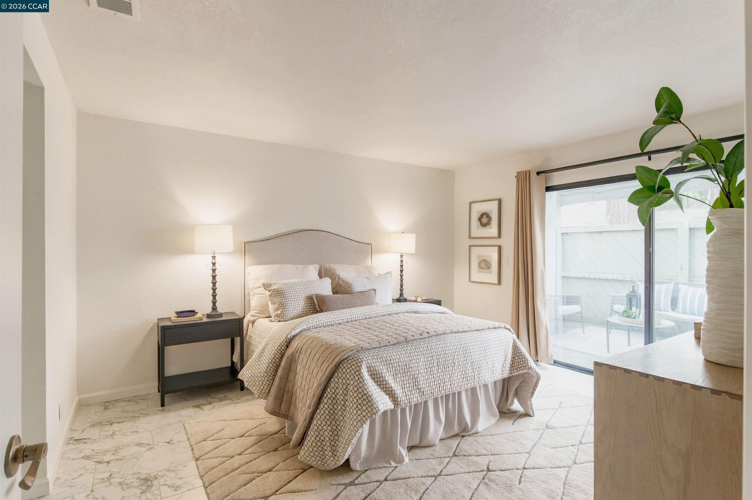 Staged bedroom with a patterned bed, marble-look tile floor, and sliding glass door to a patio.