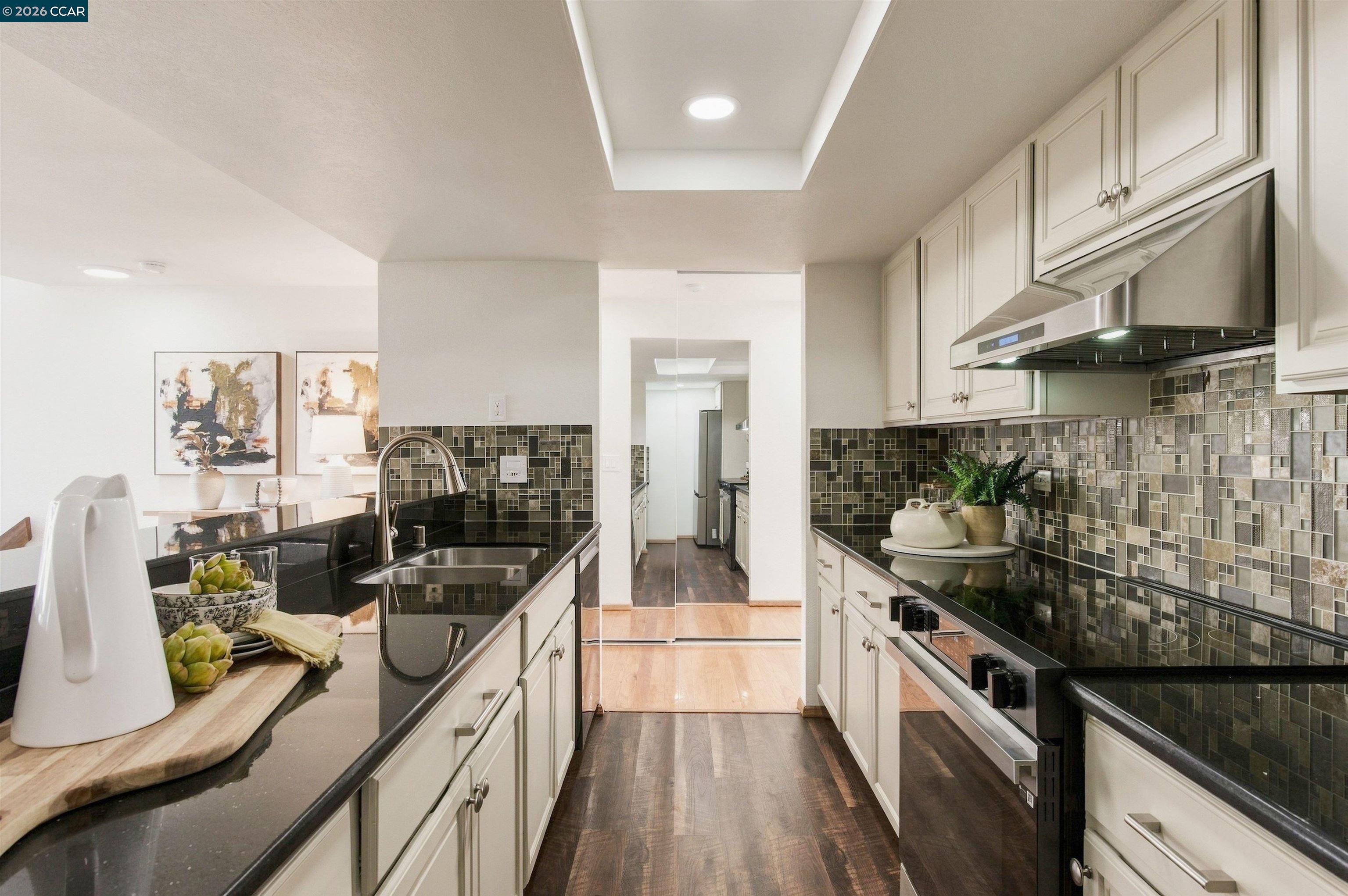 Kitchen with white cabinetry, dark counters, mosaic backsplash, and stainless steel appliances.