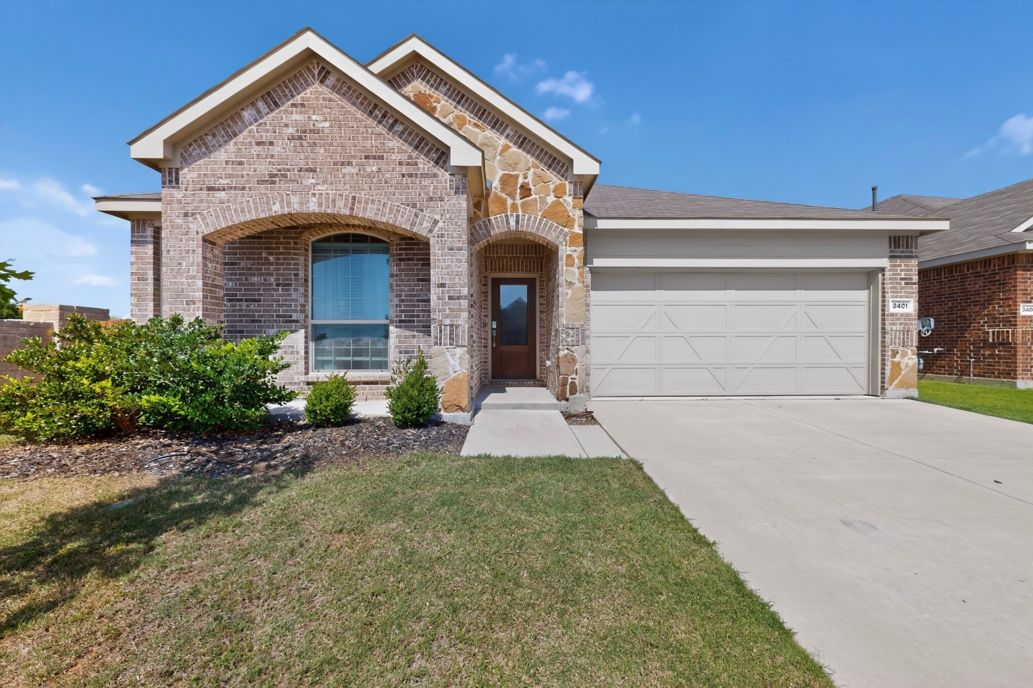 Brick-and-stone house with arched entry, white double garage door, and landscaped front yard.
