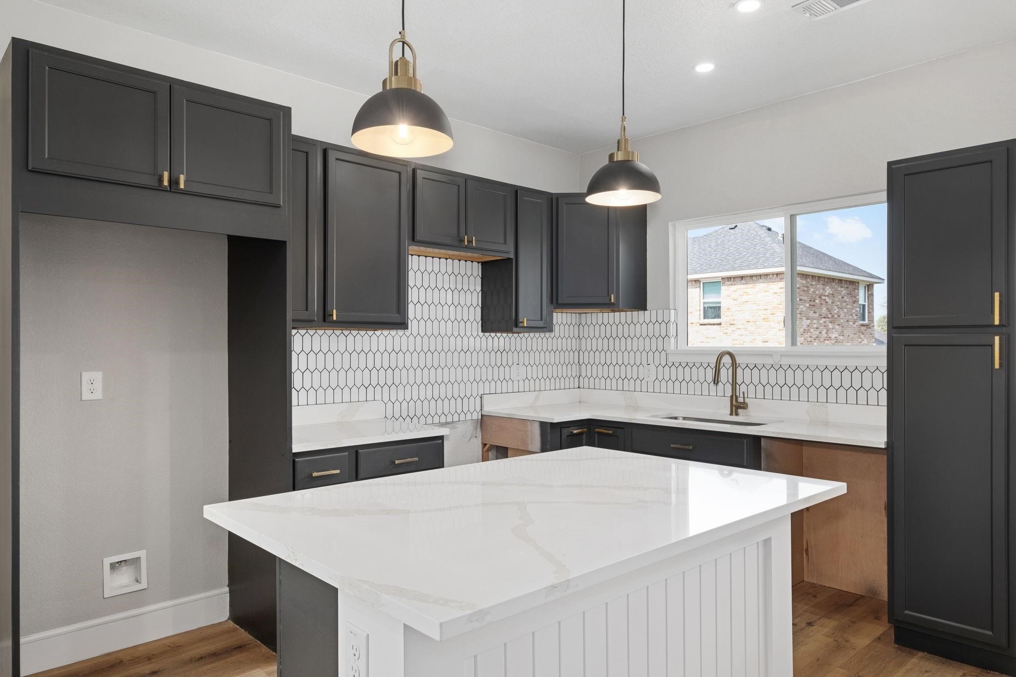 Kitchen with charcoal cabinets, geometric tile backsplash, and a large white island.