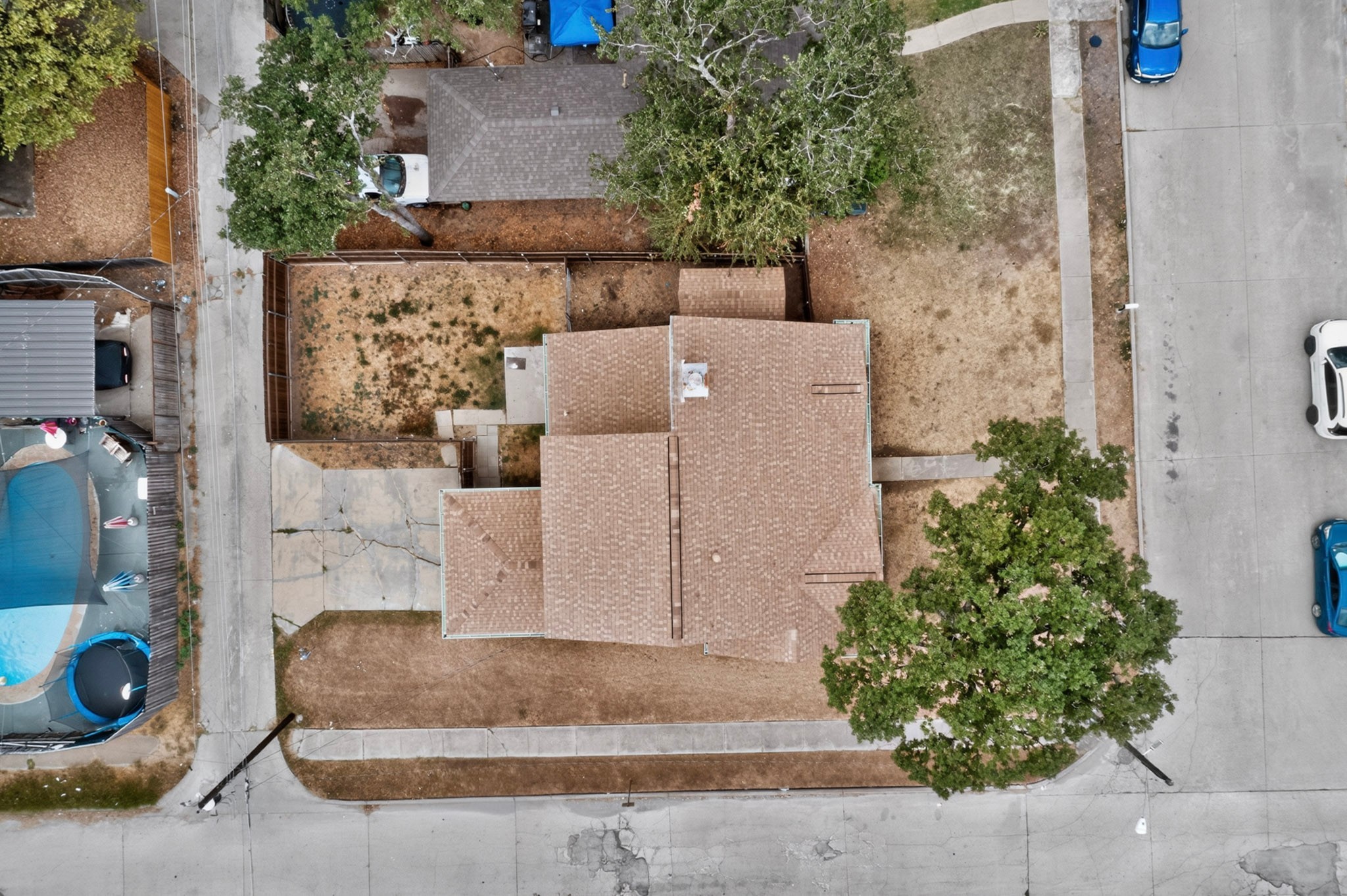 Aerial view of a single-story house with a fenced yard and a large tree by the street.