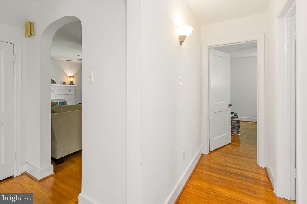 White hallway with hardwood floors, an arched living room opening, and an open doorway.