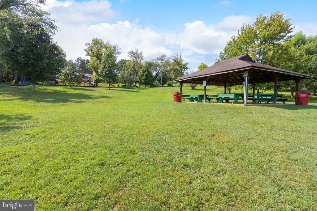 Grassy park with a covered picnic pavilion, tables, playground equipment, and mature trees.