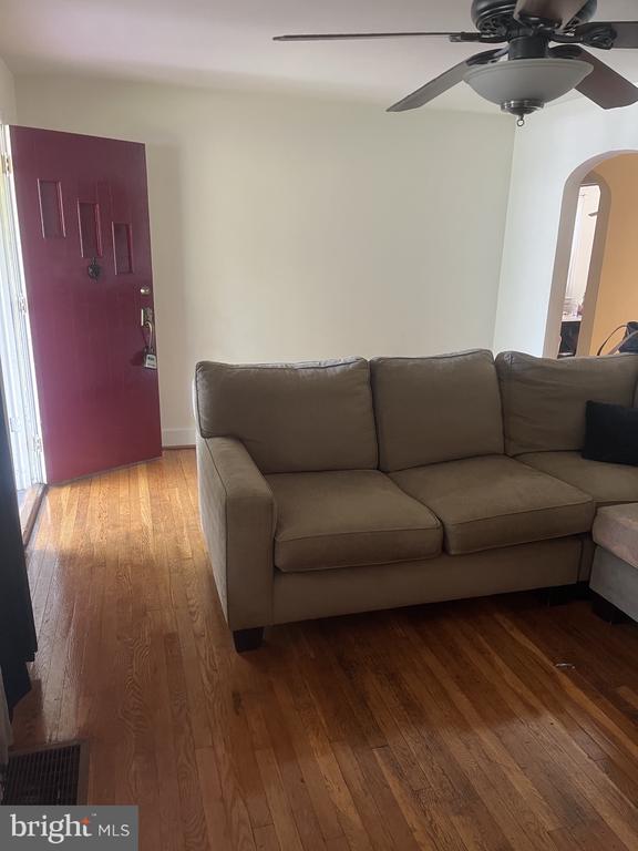 Living room with a gray sectional, hardwood floors, ceiling fan, and burgundy front door.