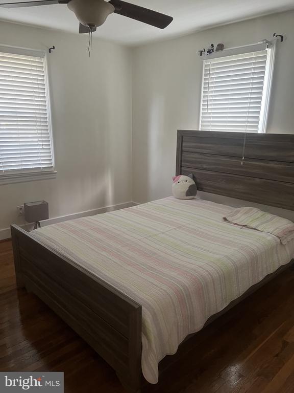 Bedroom with a dark wood bed, striped bedding, hardwood floors, and two windows with white blinds.