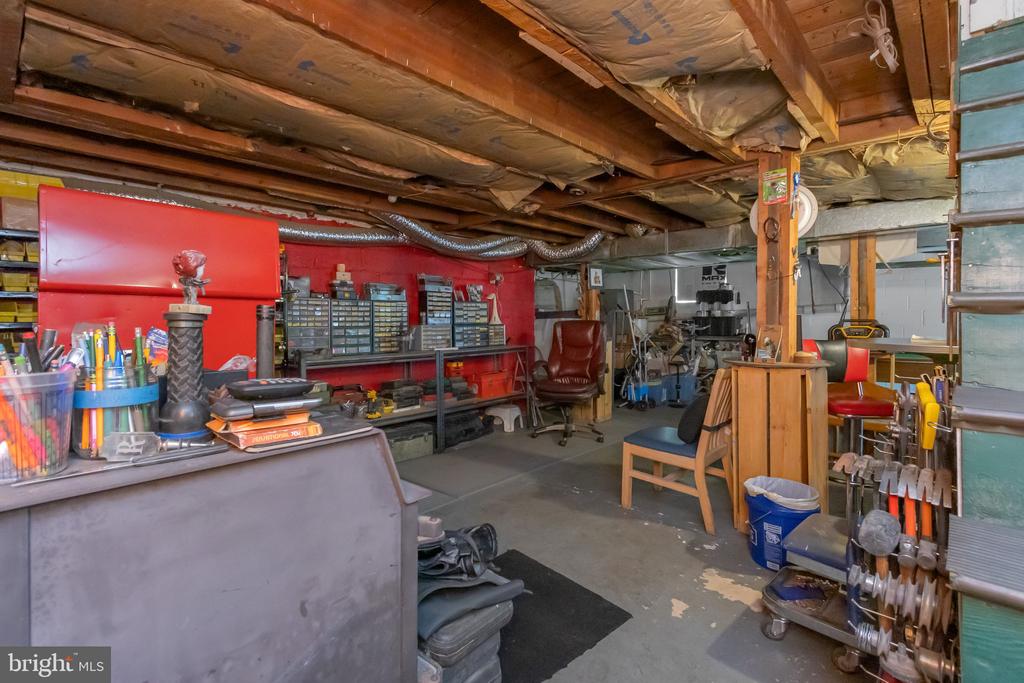 Workshop with a red tool wall, crowded workbenches, and exposed ceiling joists.