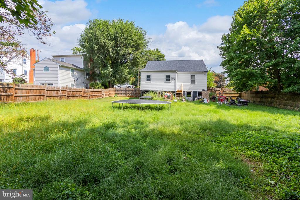 Fenced grassy backyard with a circular trampoline and the rear of a white house.