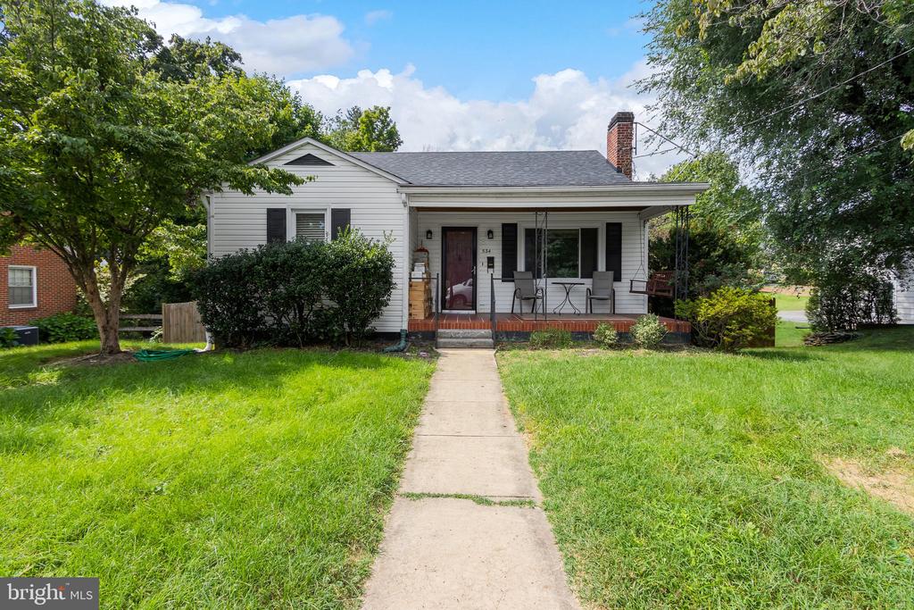 White single-story house with a covered porch, brick chimney, and concrete walkway.