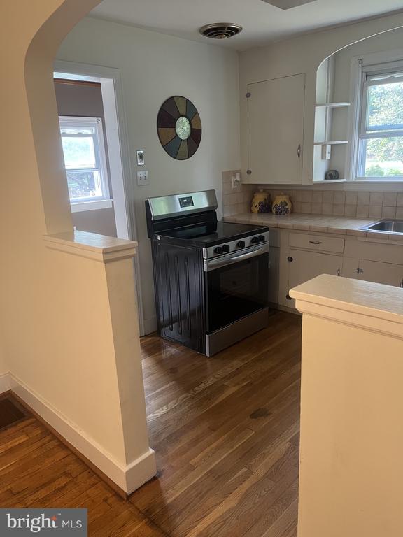 Kitchen with white cabinets, stainless steel range, wood floors, and an arched opening to a bright adjoining room.