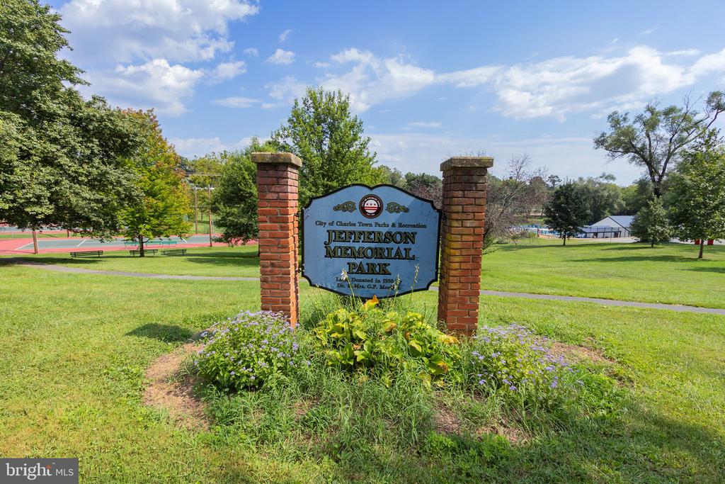 Jefferson Memorial Park sign between brick pillars, with flower beds, tennis courts, and lawns.