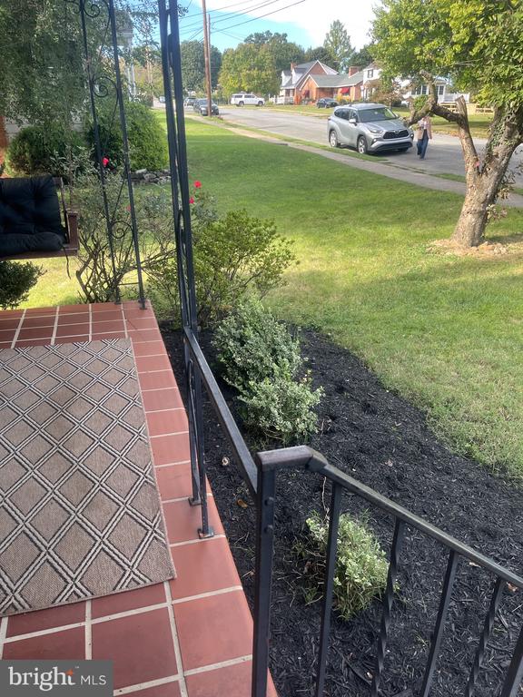 Front porch with terracotta-colored tile, black metal railings, and a view over the lawn toward the street.