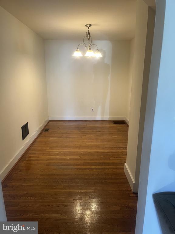 Empty dining room with polished hardwood floors and a lit chandelier.