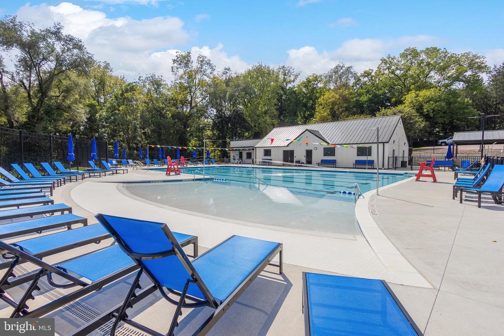Community swimming pool with a shallow entry area and blue lounge chairs beside a small pool building.