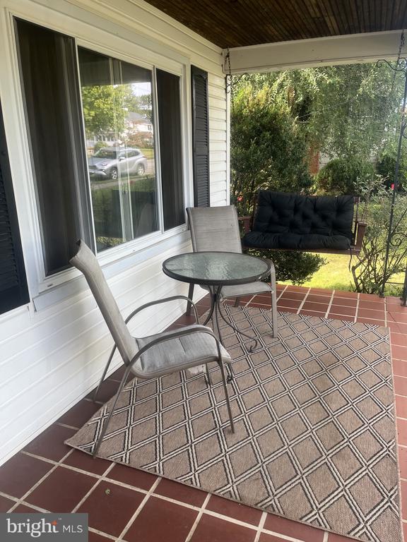 Covered porch with seating and a patterned rug, opening onto a leafy garden.