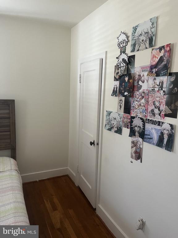Bedroom with dark hardwood floors, a partial bed, and anime posters on the wall.