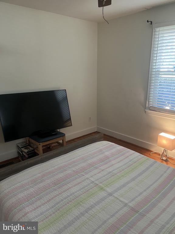 Bedroom with a pastel striped bedspread, television, and window with blinds.
