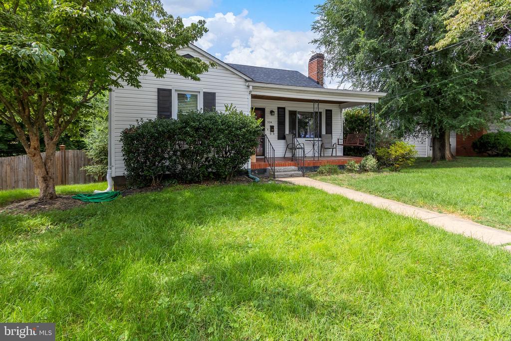 White single-story house with a covered porch, brick chimney, and tree-shaded lawn.