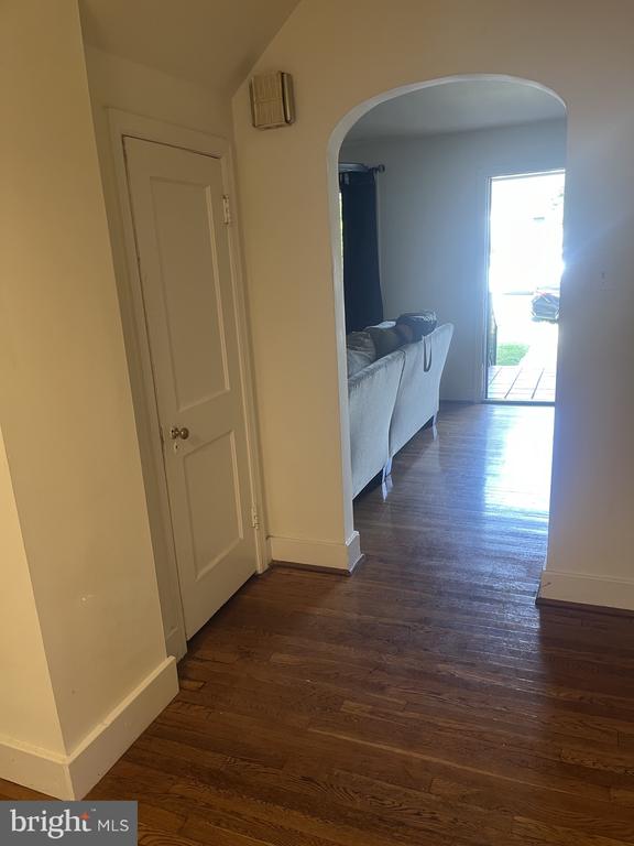 Hallway with dark hardwood floors and an arched opening to a furnished living room.