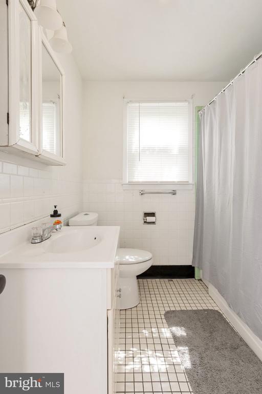 Bathroom with white vanity, toilet, tiled floor, and a curtained tub or shower.