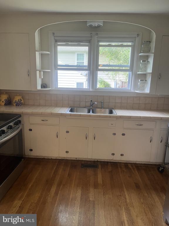Kitchen with a double sink beneath two windows, cream cabinets, and hardwood flooring.