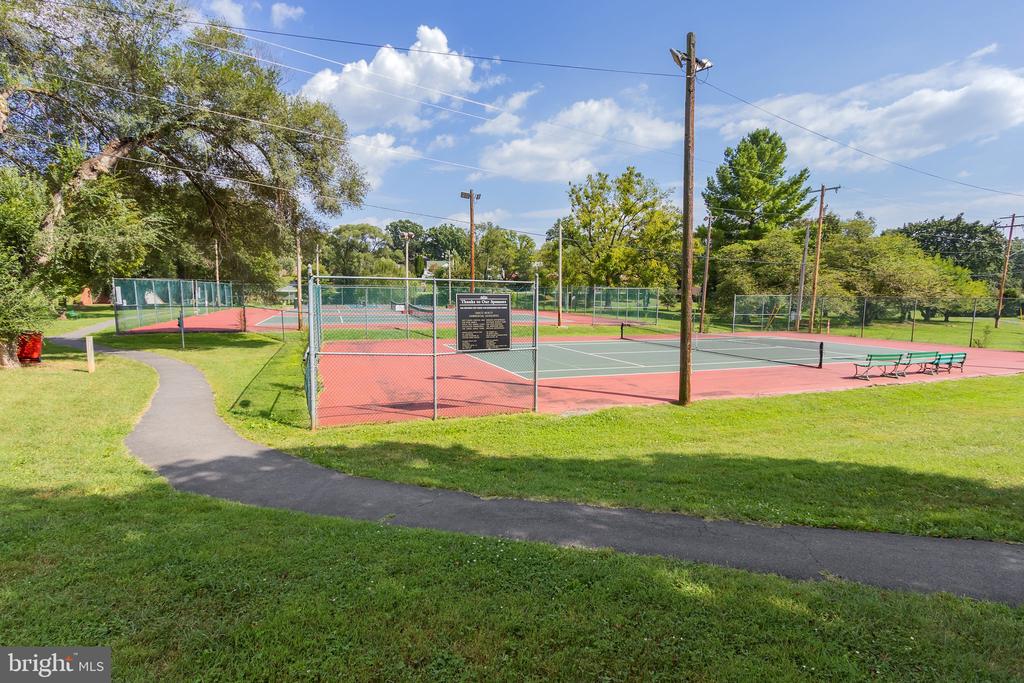 Fenced tennis courts in a grassy park, with benches and a paved path.