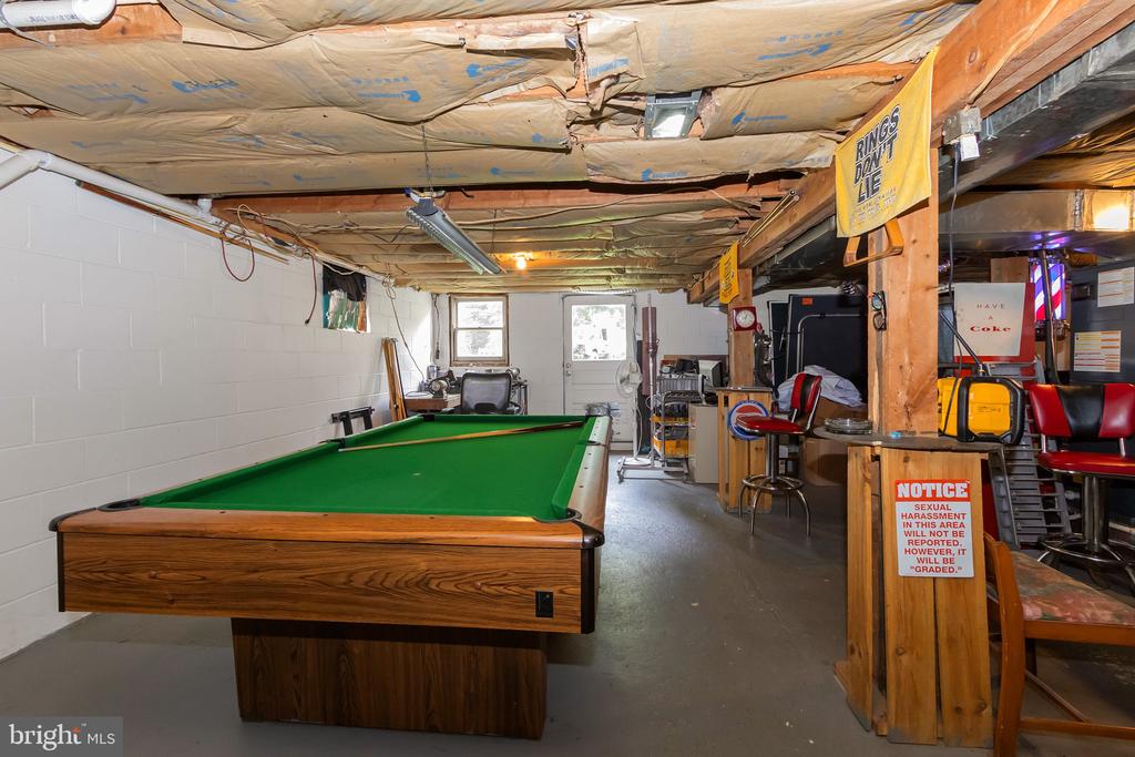 Basement recreation room with a green-felt pool table, exposed ceiling insulation, and bar stools.