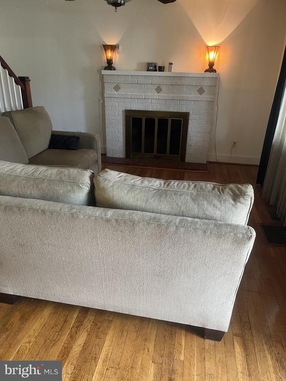 Living room with a white brick fireplace, glowing sconces, light sofas, and hardwood floors.