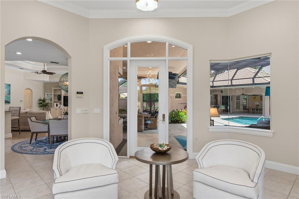 Living room with white armchairs overlooking a covered lanai and pool.