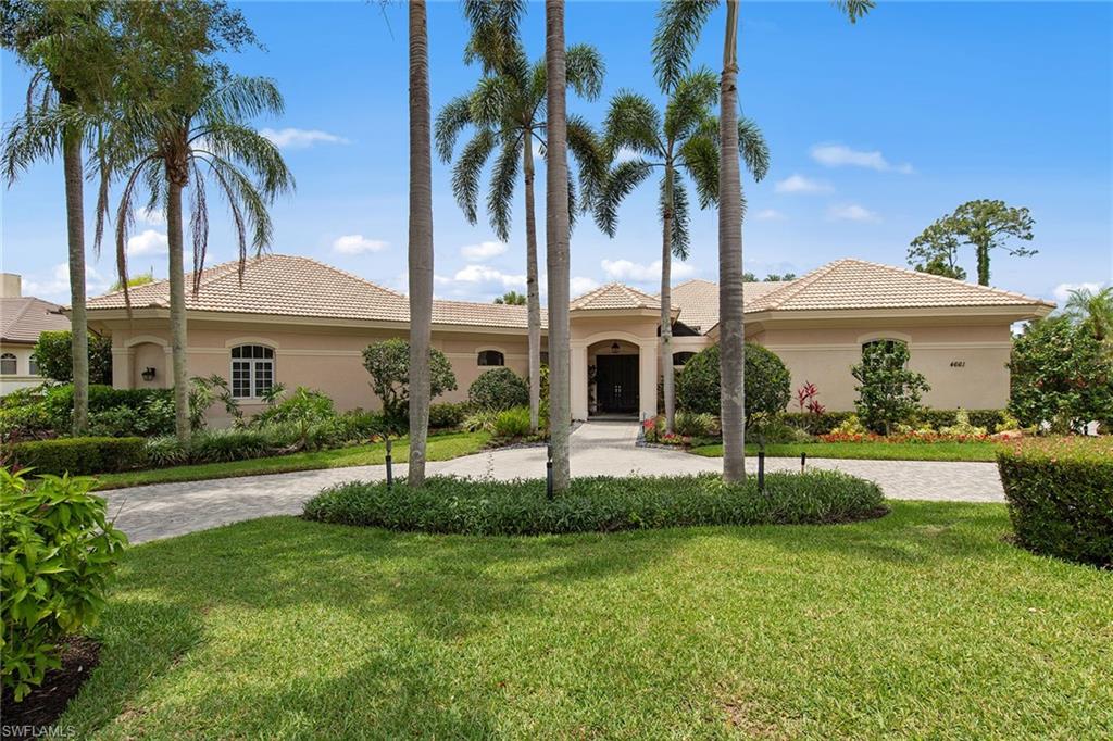 Beige single-story home with a tiled roof, curved driveway, and tall palms.