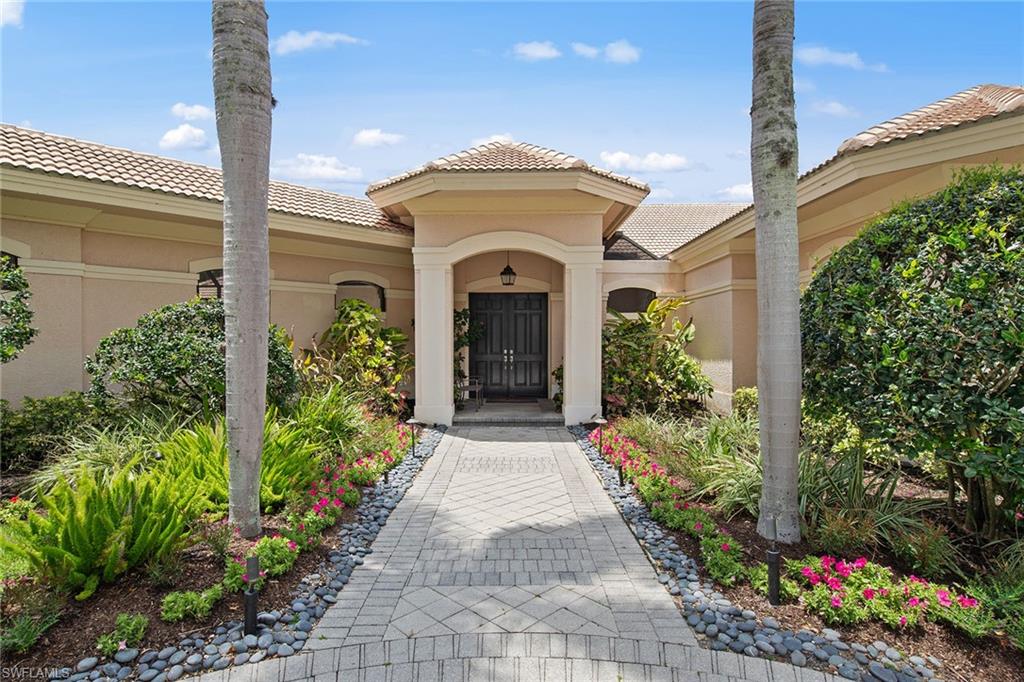 Home entrance with a paved walkway, tropical landscaping, and pink flowers.